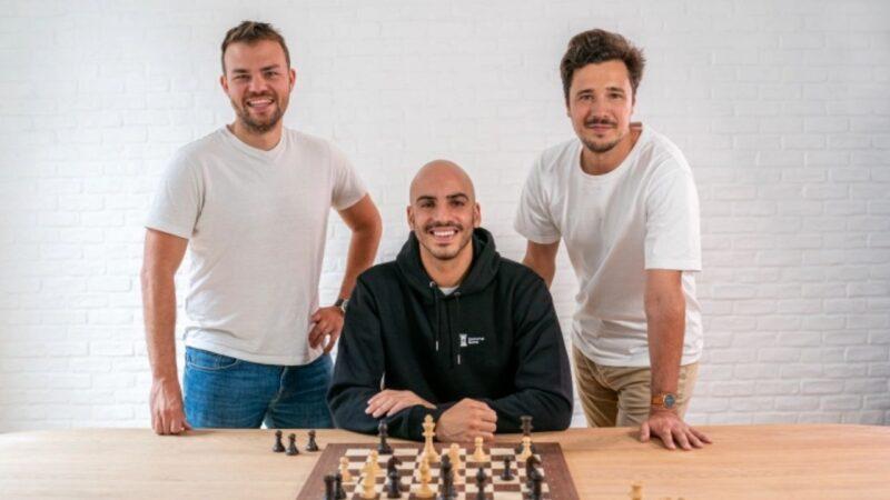 Masa üzerinde bir satranç tahtası ve arkada Immortal Game kurucu ortakları